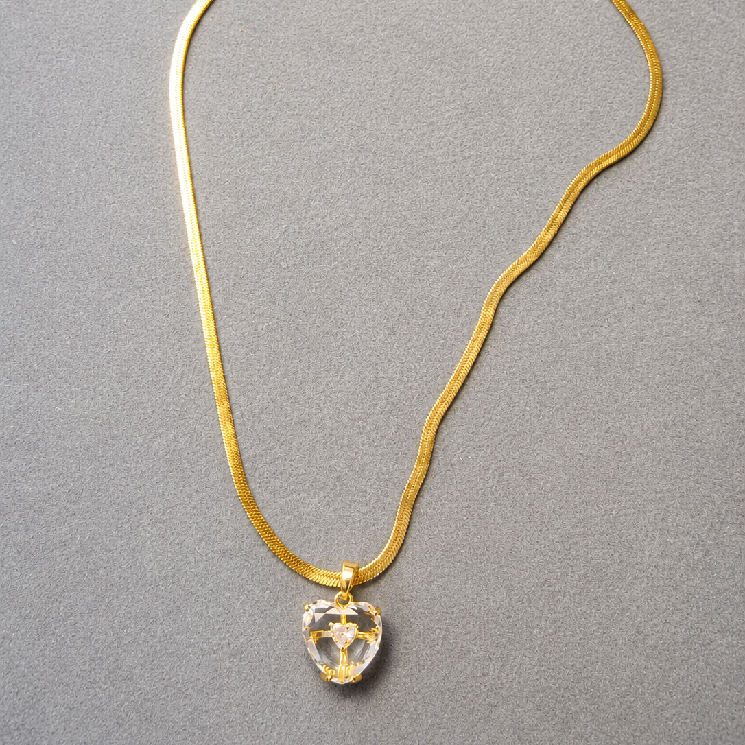 Gold tone necklace with a clear crystal pendant on a gray background