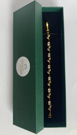 A gold leaf-patterned bracelet with clear rhinestones displayed inside an open dark green presentation box with a black velvet interior.