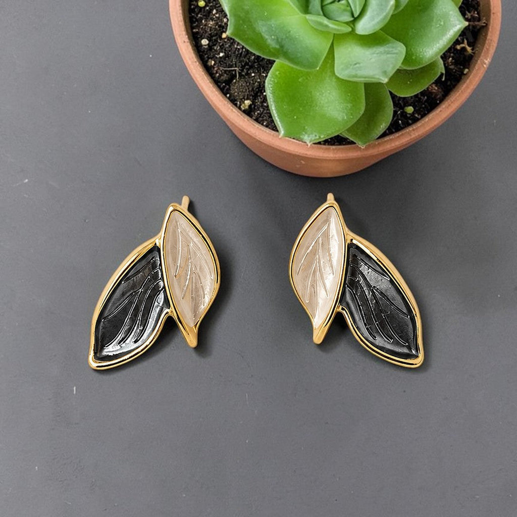 Pair of leaf-shaped earrings on a dark surface with a potted succulent in the background.