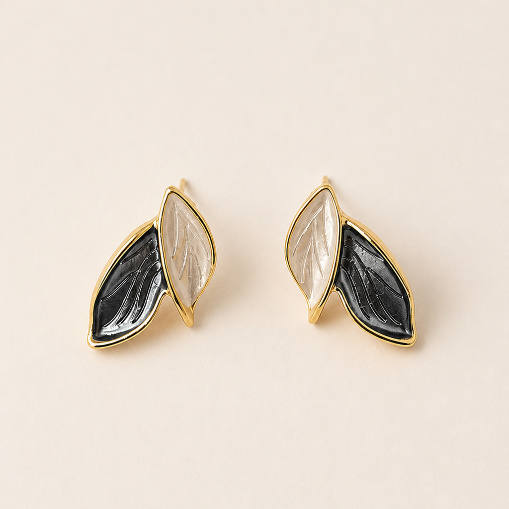 Pair of gold earrings with black and gray stone-like designs on a beige background