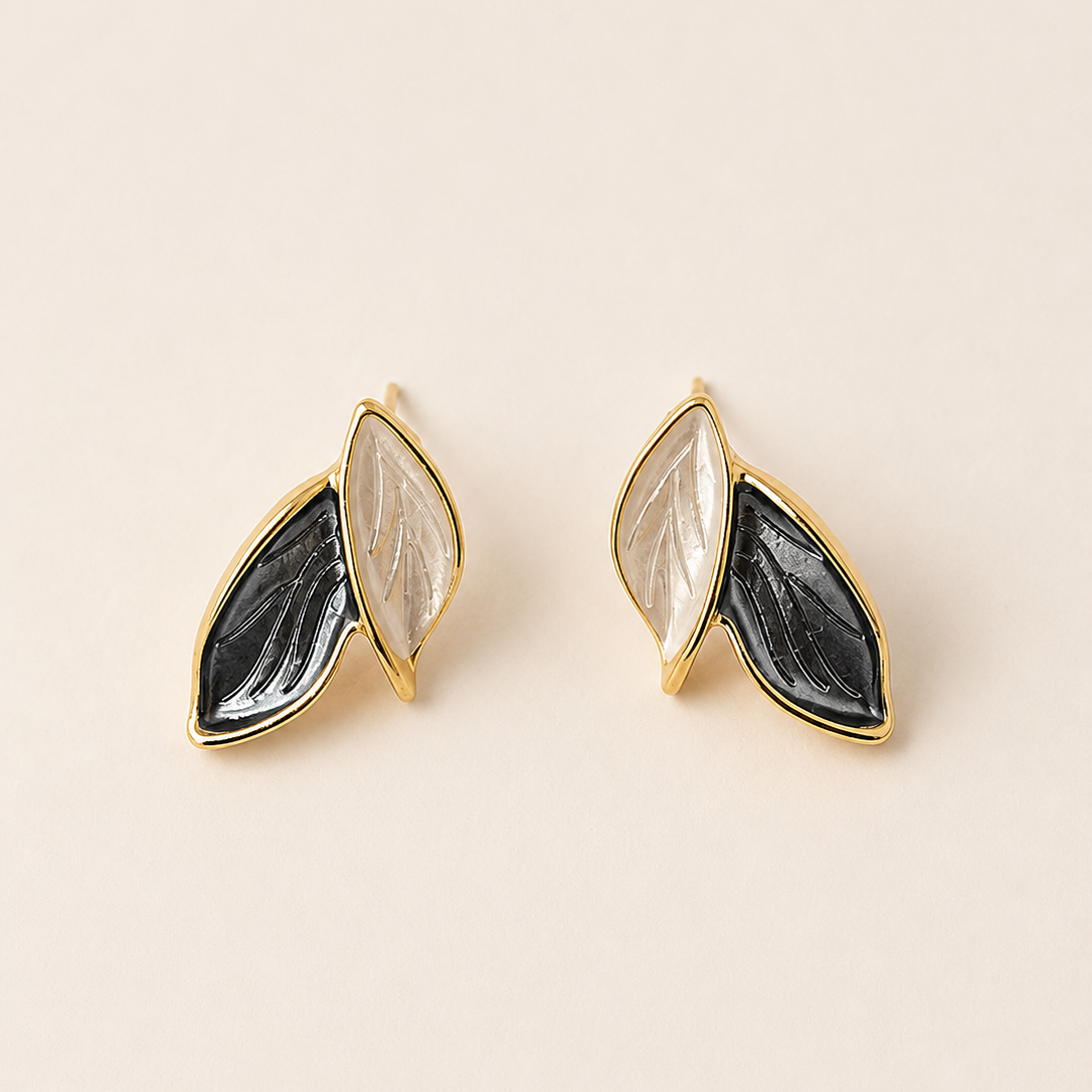 Pair of gold earrings with black and gray stone-like designs on a beige background