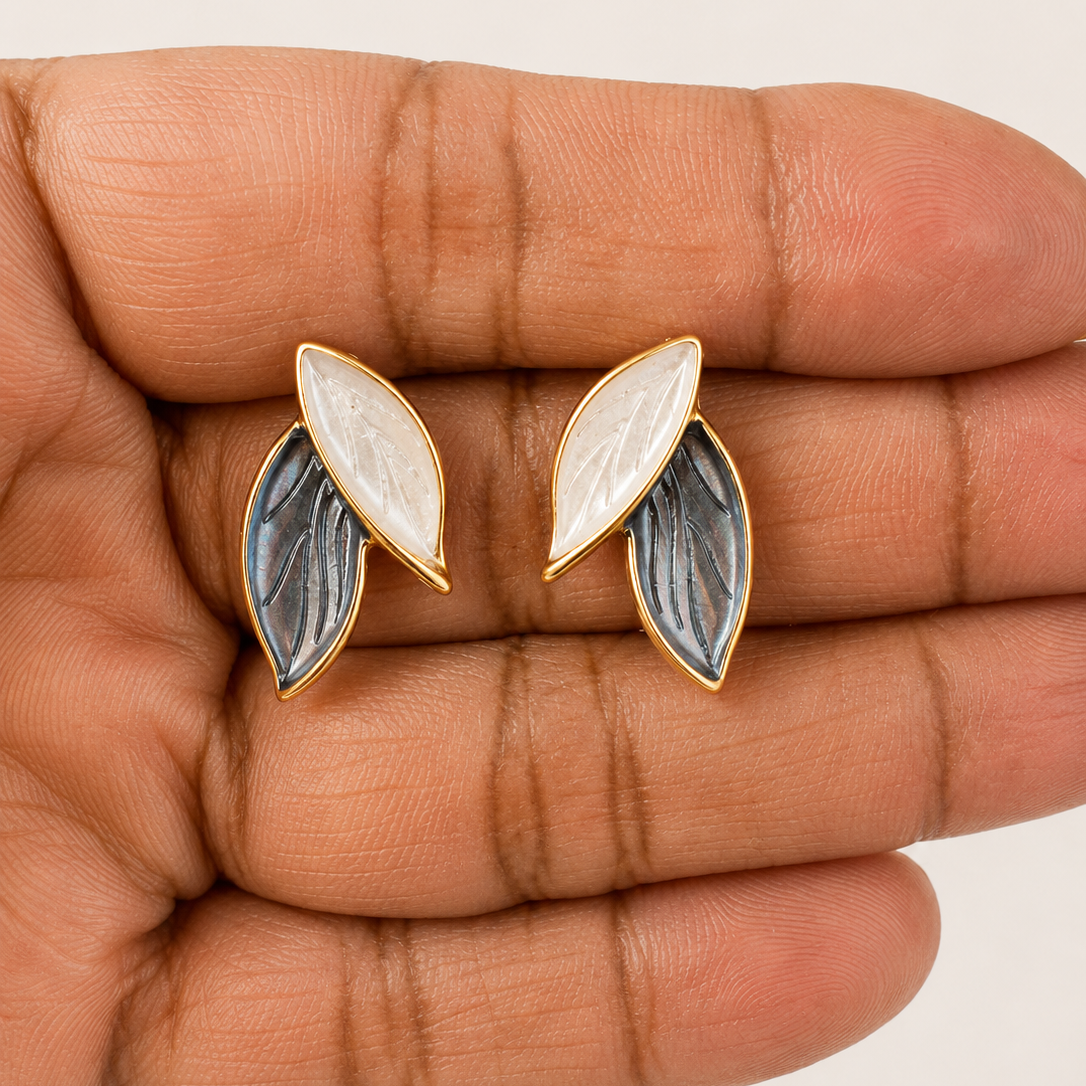 Pair of leaf-shaped earrings held between fingers on a light background