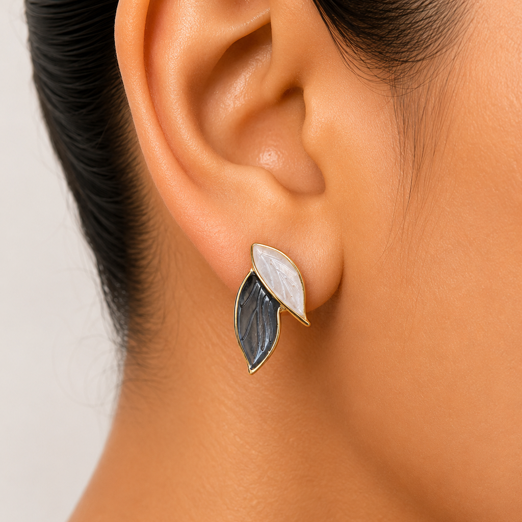 Close-up of an ear wearing a leaf-shaped earring with a white and black design.