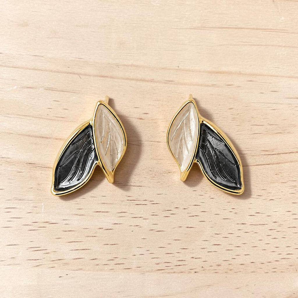Pair of gold-framed earrings with black and white design on a wooden surface