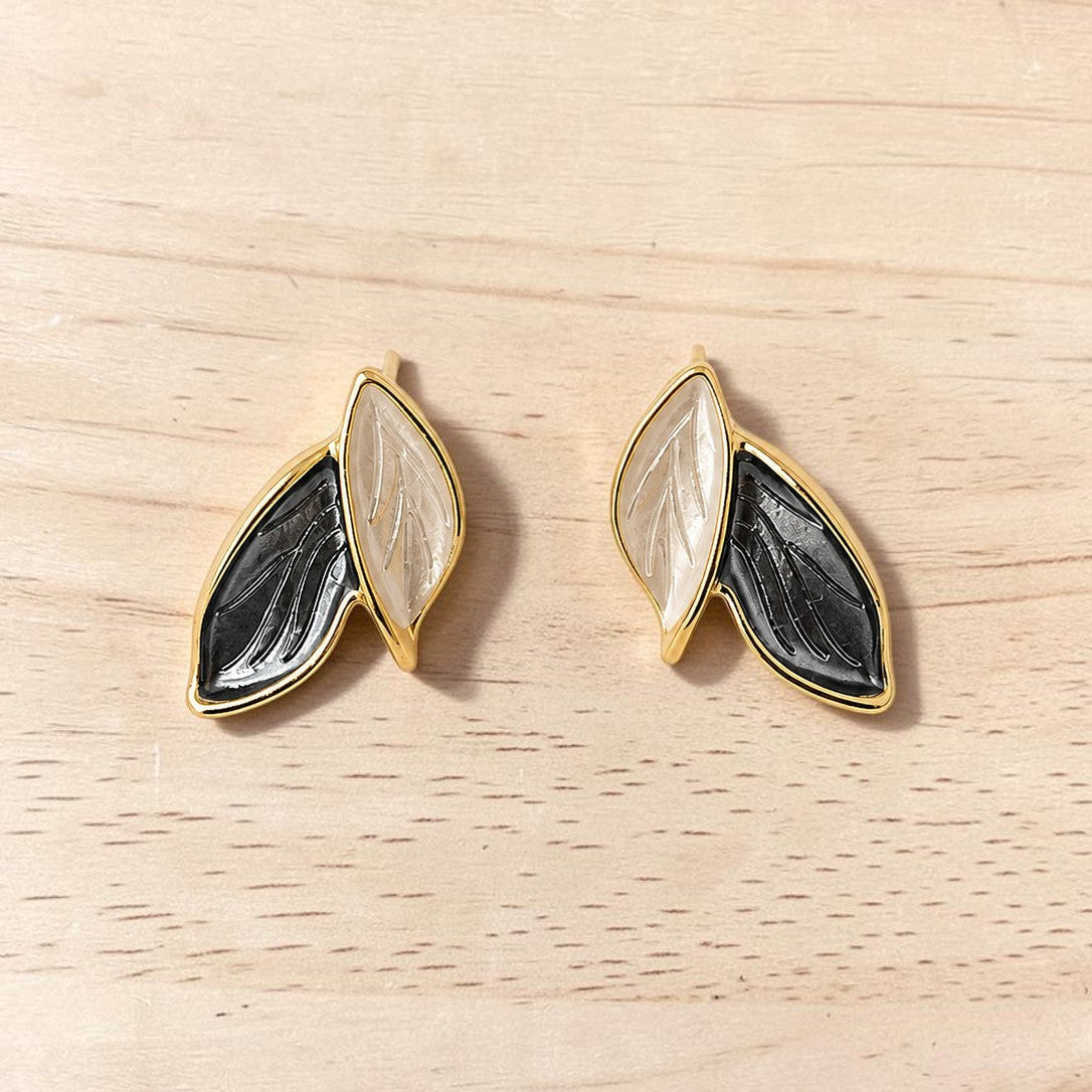 Pair of gold-framed earrings with black and white design on a wooden surface