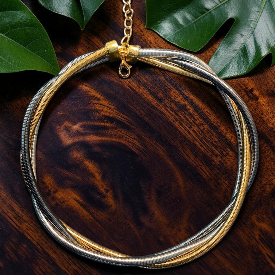 Gold and silver necklace on a wooden surface with green leaves