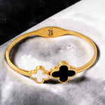 Gold tone bracelet with clover-shaped charms on a textured surface