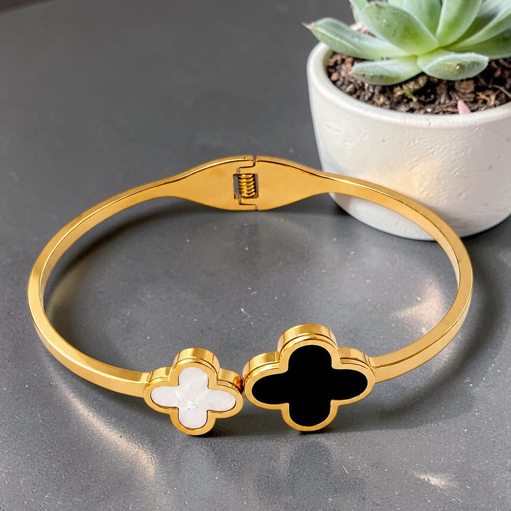 Gold tone bracelet with clover designs on a gray surface with a succulent plant in the background