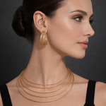Woman wearing gold tone necklaces and earrings against a dark background
