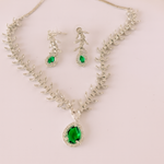 Jewelry set with necklace and earrings featuring green gemstones on a light pink background