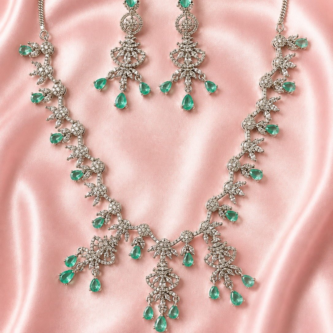 Jewelry set with necklace and earrings featuring green gemstones on a pink satin background