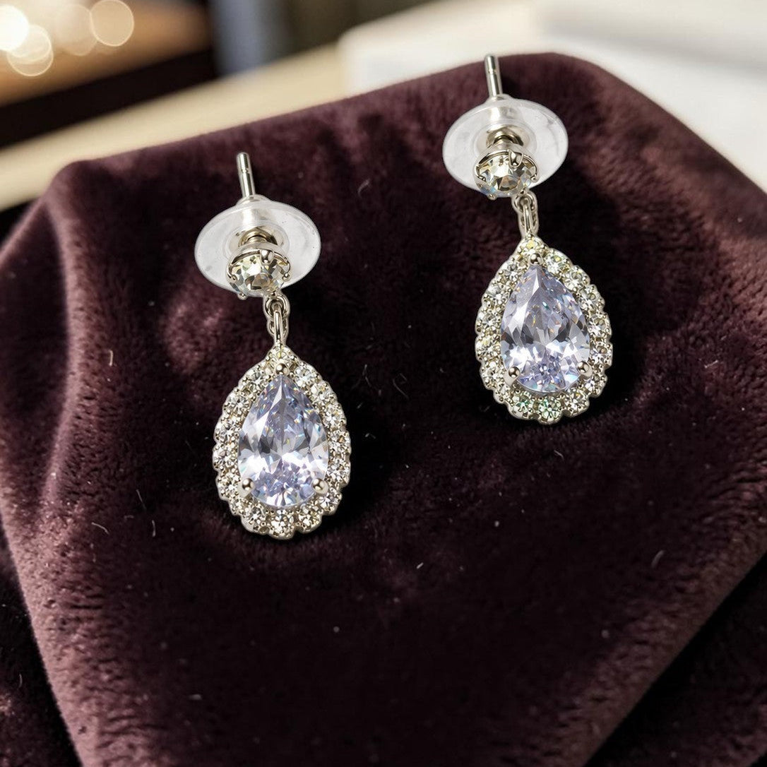 Teardrop-shaped earrings with clear gemstones on a brown velvet surface.