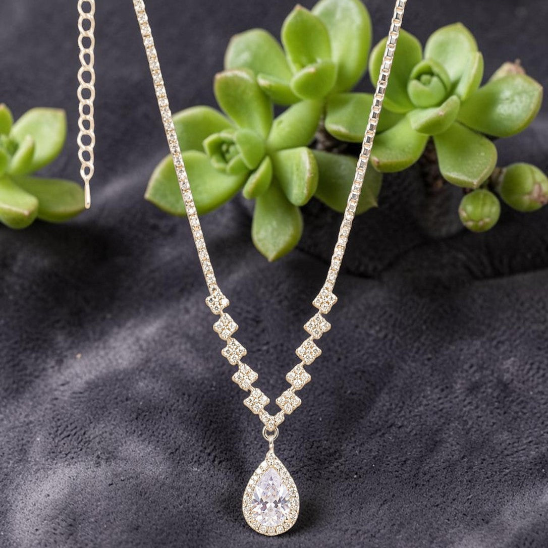 AmericanDiamond necklace with a teardrop pendant on a dark surface with green succulents.