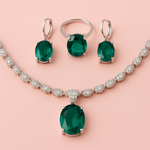 Jewelry set with emerald green gemstones on a pink background