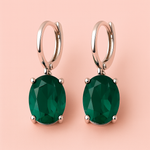 Pair of green gemstone earrings with rose gold hooks on a pink background