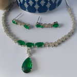 Jewelry set with green gemstones and silver accents on a white surface.