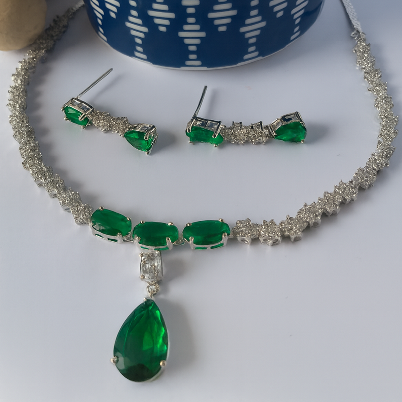 Jewelry set with green gemstones and silver accents on a white surface.