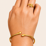 Gold tone bracelet and ring on a hand against a beige background