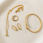 Set of gold tone jewelry including a bracelet, ring, and earrings on a beige background