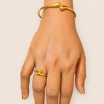 Hand wearing a gold bracelet and ring on a plain background
