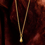 Golden necklace with a teardrop pendant on a brown textured surface