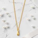 Golden necklace with a teardrop pendant on a marble surface with scattered pearls.