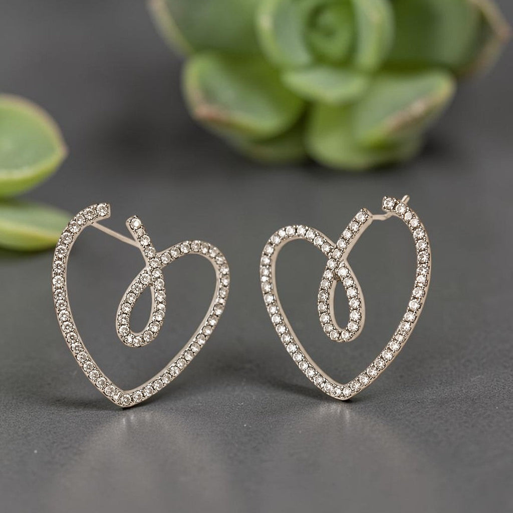Heart-shaped earrings with sparkling stones on a gray surface with green plants in the background
