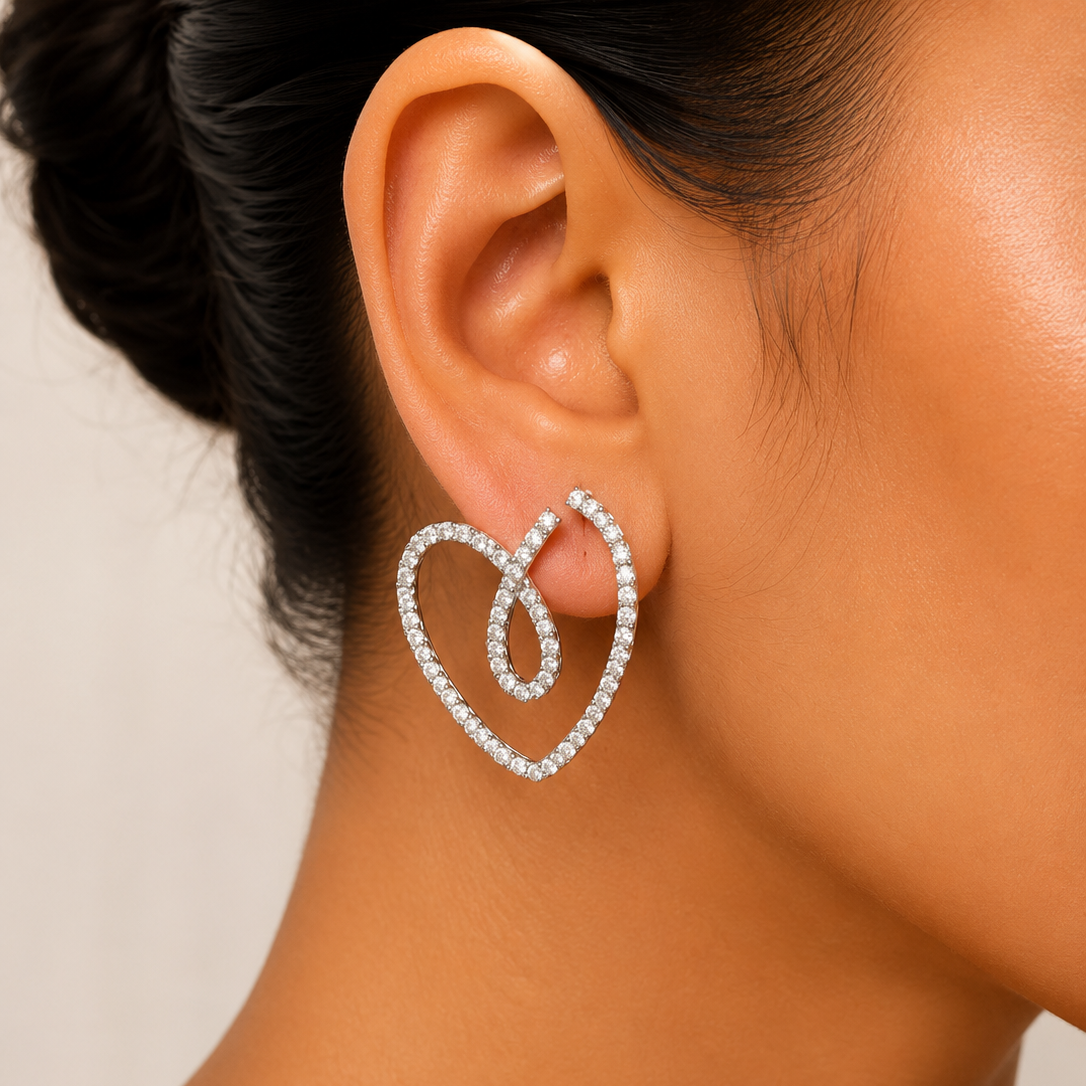 Heart-shaped earrings being worn on an ear with a neutral background