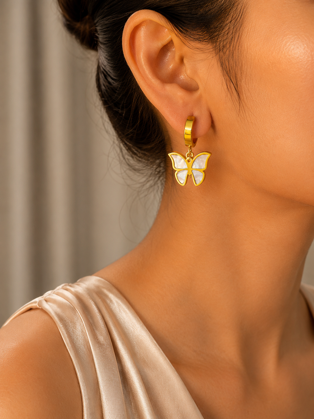 Golden earring with a butterfly design worn by a person against a neutral background