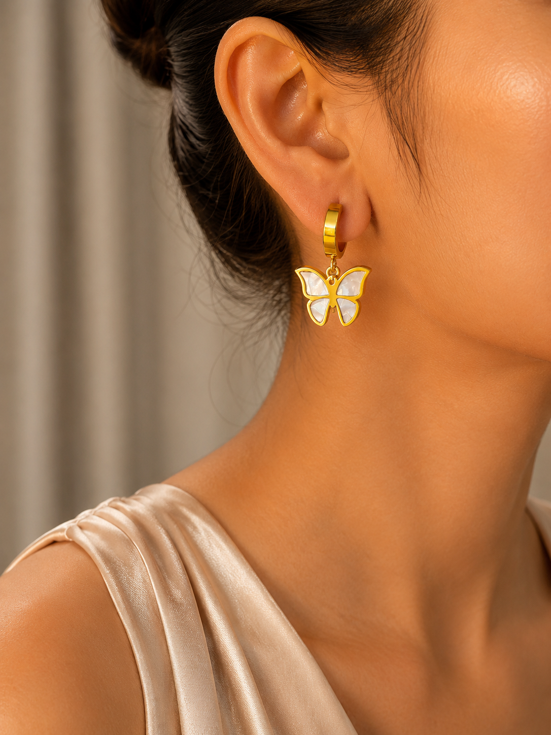 Golden earring with a butterfly design worn by a person against a neutral background