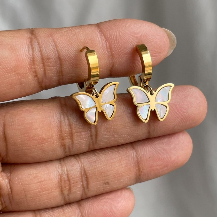 Golden butterfly earrings held between fingers against a neutral background