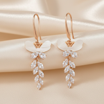 Rose gold tone earrings with diamond-like stones on a beige satin background