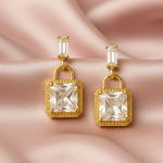 Gold tone earrings with clear gemstones on a pink satin background