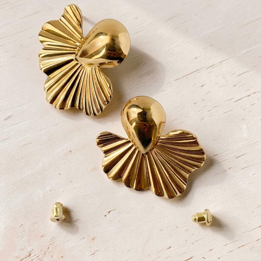Pair of gold shell-shaped earrings on a light wooden surface