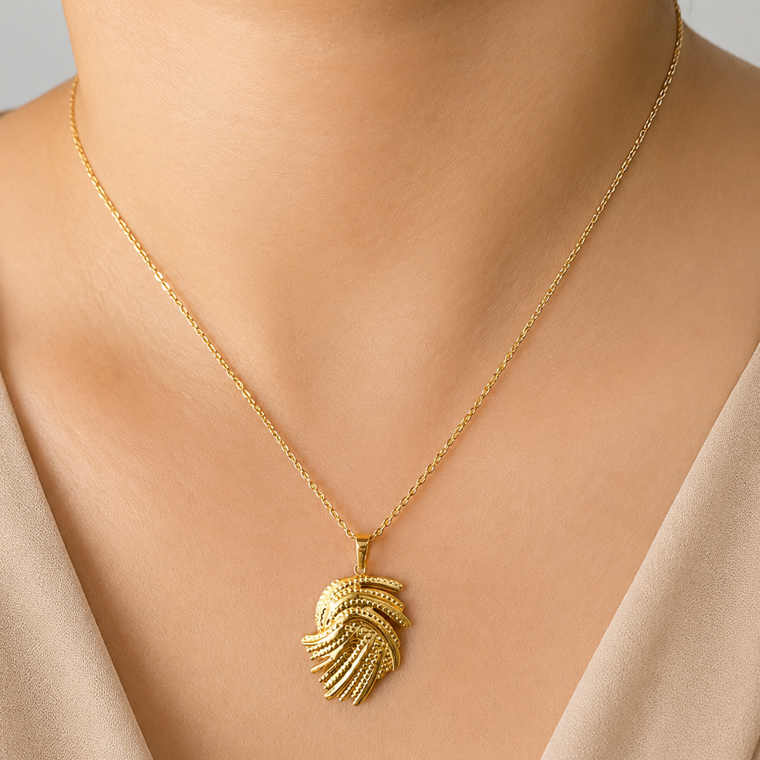 Gold tone necklace with a leaf-shaped pendant on a neutral background