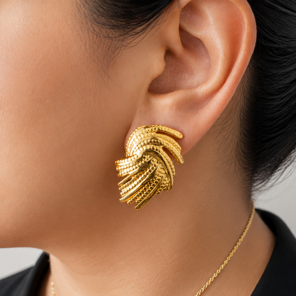 Gold tone earrings and necklace on a person against a neutral background