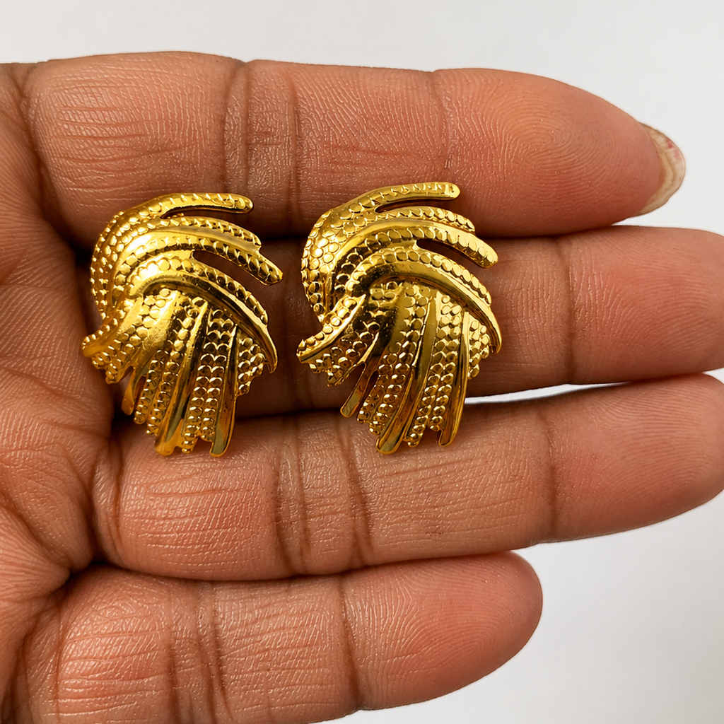 Gold tone earrings held between fingers against a neutral background