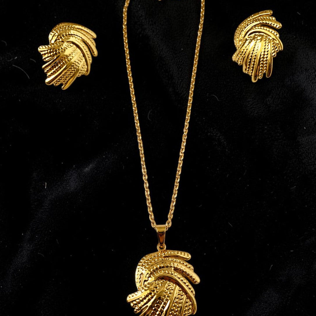 Gold tone necklace with a large pendant and matching earrings on a black background