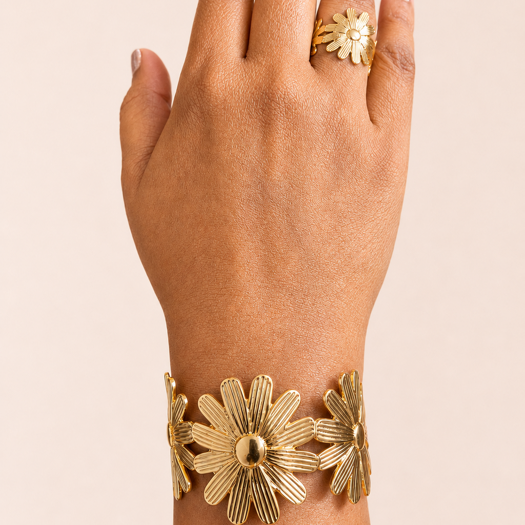 Hand wearing a gold tone bracelet and ring with floral designs on a beige background