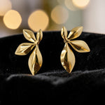 Gold leaf-shaped earrings on a black cushion with a blurred gold light background