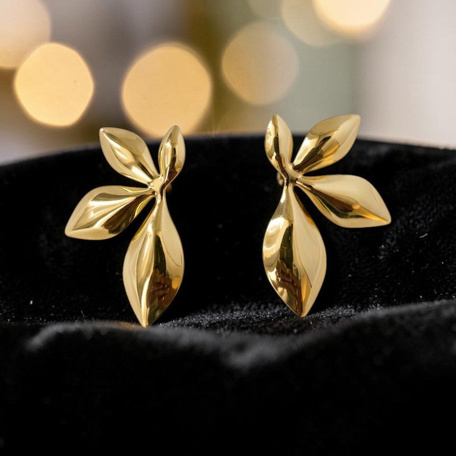 Gold leaf-shaped earrings on a black cushion with a blurred gold light background