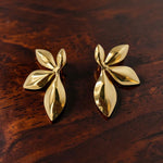 Pair of gold leaf-shaped earrings on a wooden surface