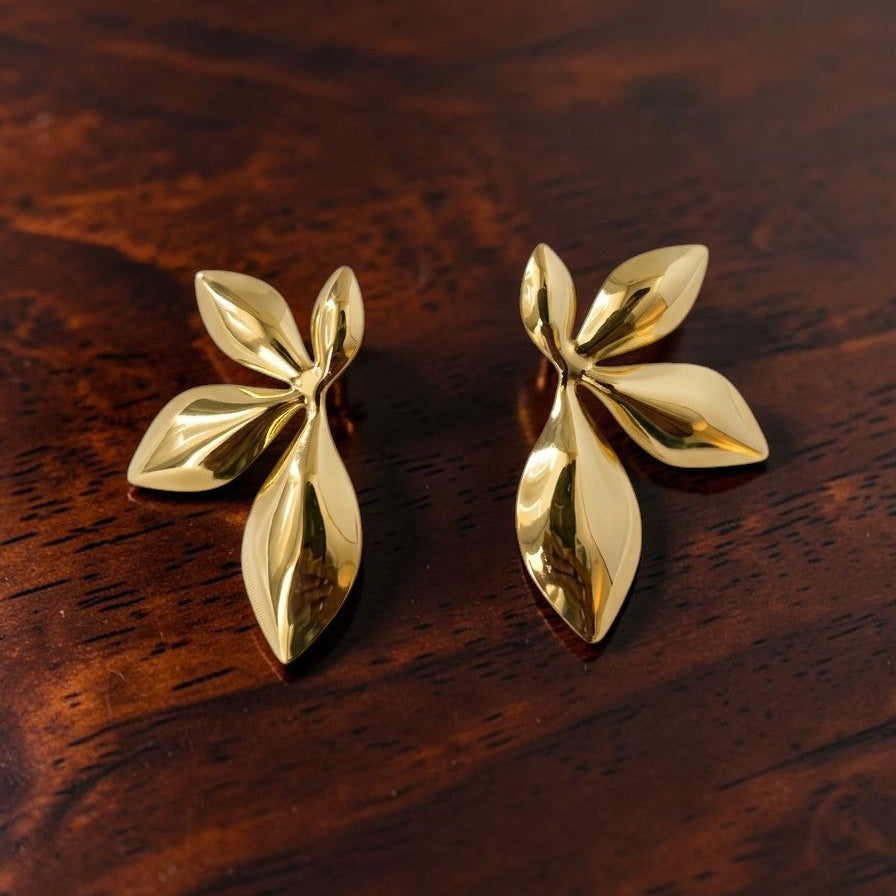 Pair of gold leaf-shaped earrings on a wooden surface