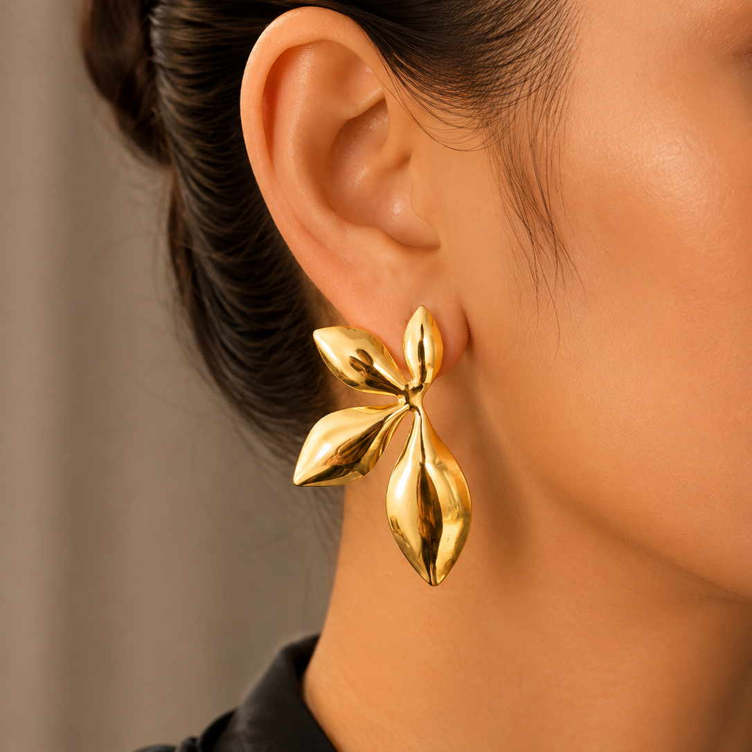 Gold leaf-shaped earring worn by a person with a neutral background