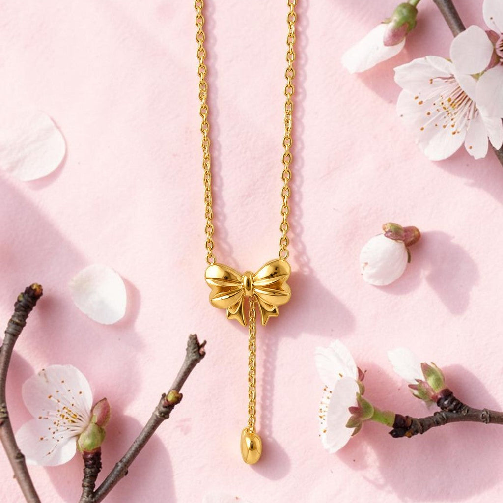 Gold tone bow-shaped necklace on a pink background with cherry blossom branches