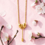 Gold tone bow-shaped necklace on a pink background with cherry blossom branches