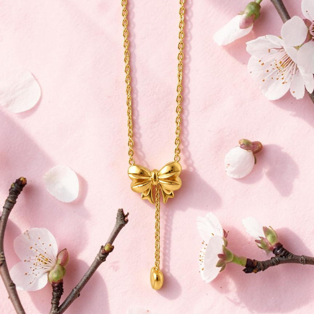 Gold tone bow-shaped necklace on a pink background with cherry blossom branches