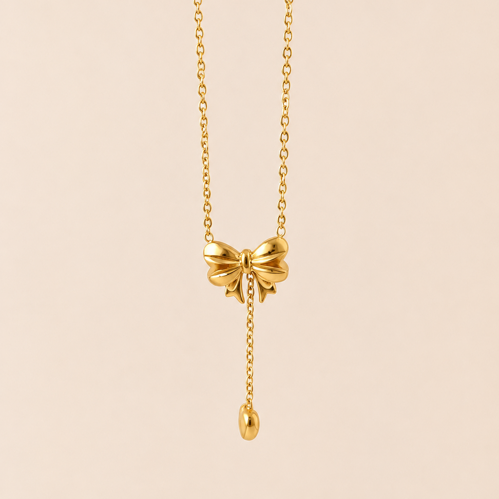 Gold tone necklace with a bow pendant on a beige background
