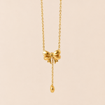 Gold tone necklace with a bow pendant on a beige background
