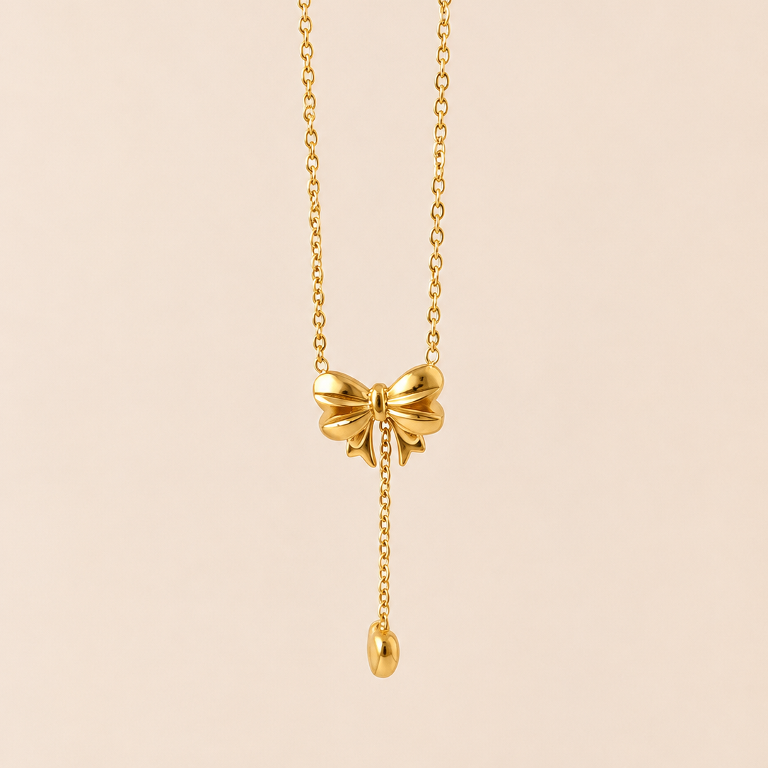 Gold tone necklace with a bow pendant on a beige background